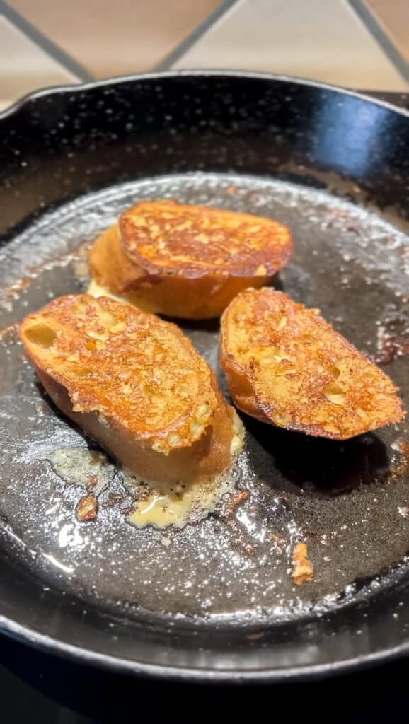 Portrait photo of 3 slices of Baguette French Toast soaked in a mascarpone custard lightly fried in a cast iron skillet.