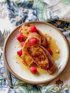 Portrait photo of finished dish of Baguette French Toast with Mascarpone Custard Recipe. The dish is garnished with fresh raspberries and maple syrup.