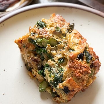 Portrait image of a slice of the Breakfast Strata for Two that's generously served on a wide rimmed ceramic plate.