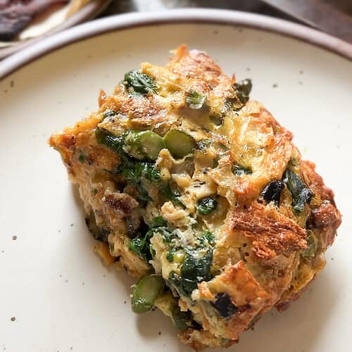 Portrait image of a slice of the Breakfast Strata for Two that's generously served on a wide rimmed ceramic plate.