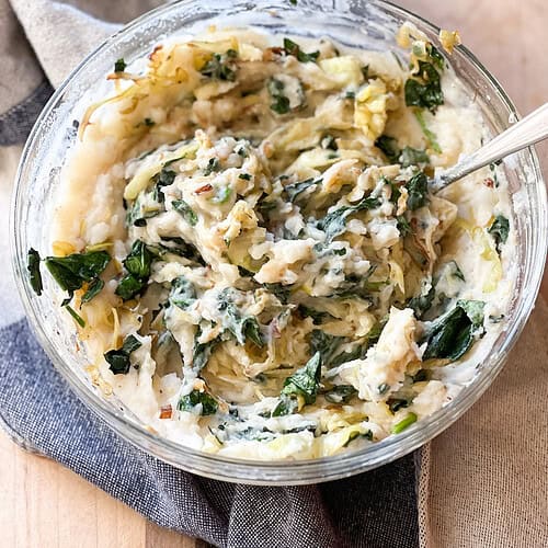 Portrait of the finished side dish: Brown Butter Colcannon with Cabbage, Spinach, and Leeks. Served in a large bowl accented with a kitchen towel.