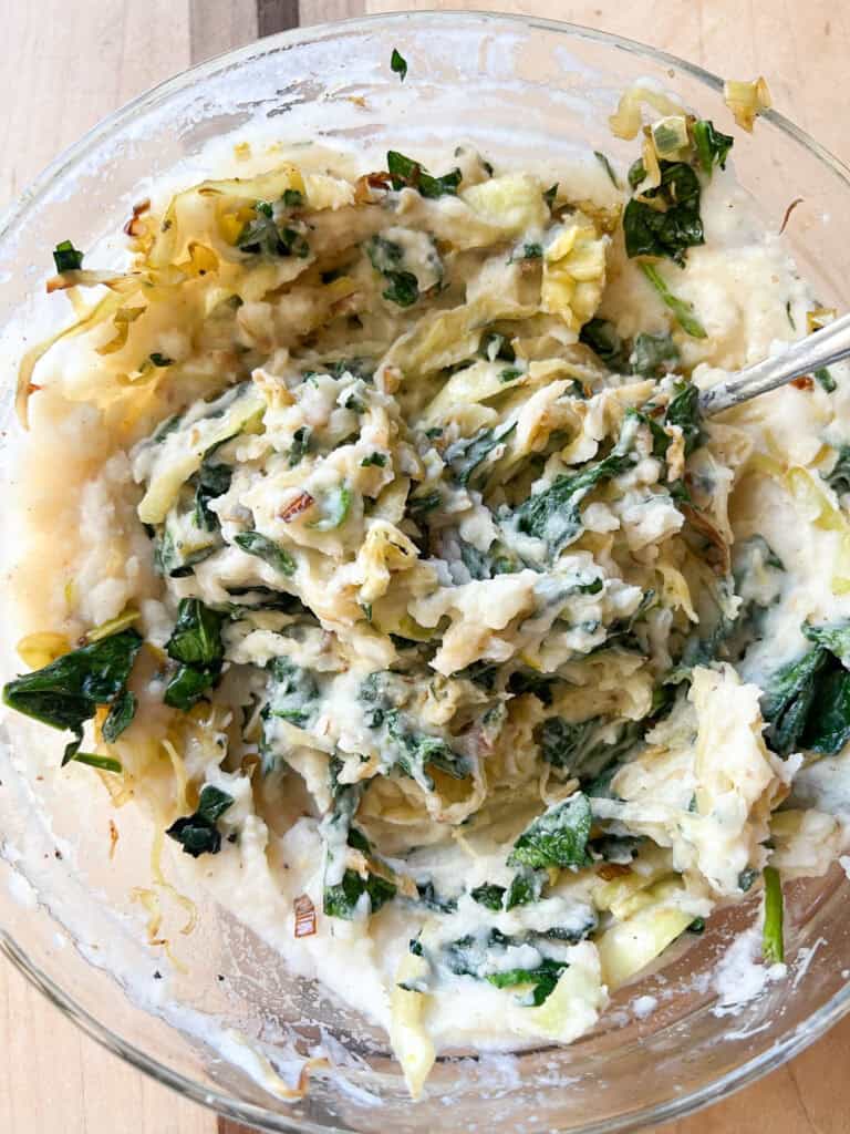 Portrait of the finished side dish: Brown Butter Colcannon with Cabbage, Spinach, and Leeks. Served in a large bowl accented with a kitchen towel.