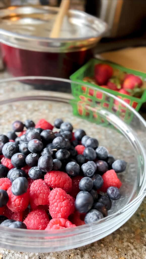 Portrait photo of a clear glass bowl filled with raspberries and blueberries in preparation for its transformation into a Mixed Berry and Raspberry Compote Recipe.