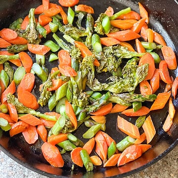 Flatlay image of roasted carrots and asparagus recipe with rabe fresh from the oven served in a cast iron skillet.