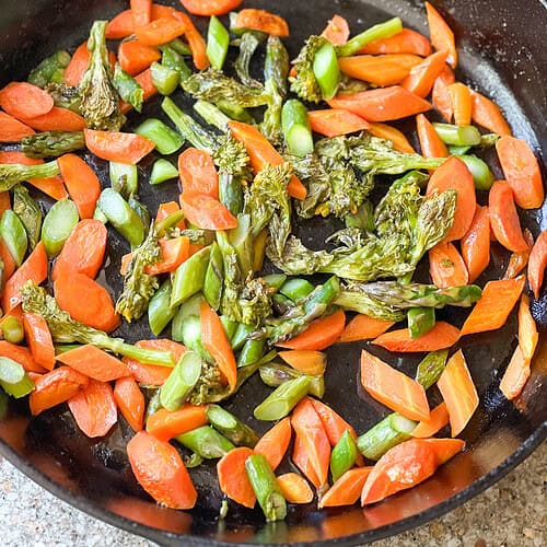 Flatlay image of roasted carrots and asparagus recipe with rabe fresh from the oven served in a cast iron skillet.