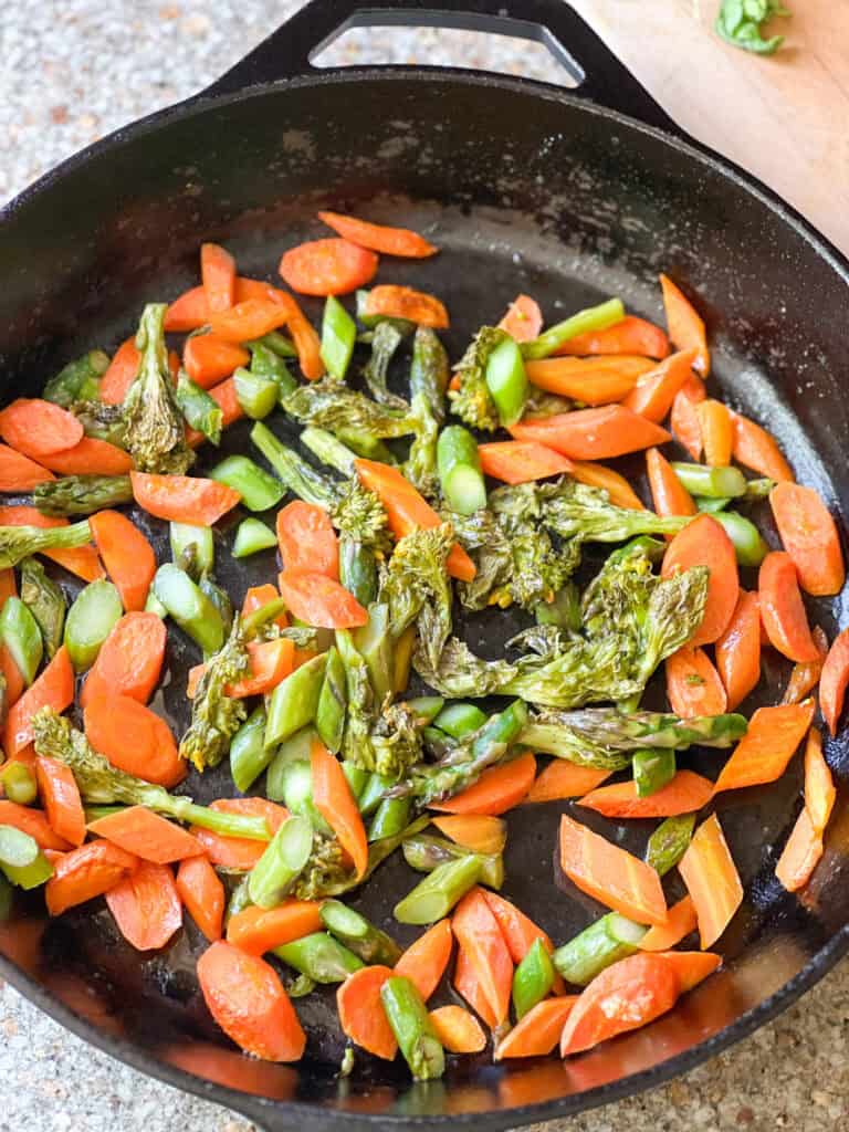 Flatlay image of roasted carrots and asparagus recipe with rabe fresh from the oven served in a cast iron skillet.