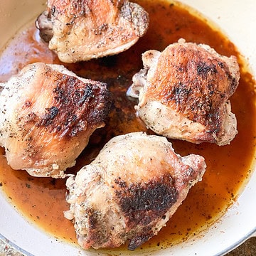 Portrait photo of 4 bone-in chicken thighs with skin on that have been roasted until crisp and golden brown for this French Roast Chicken Recipe.