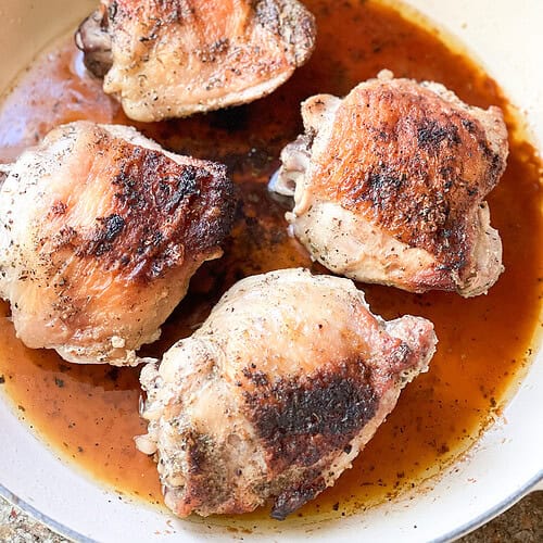 Portrait photo of 4 bone-in chicken thighs with skin on that have been roasted until crisp and golden brown for this French Roast Chicken Recipe.