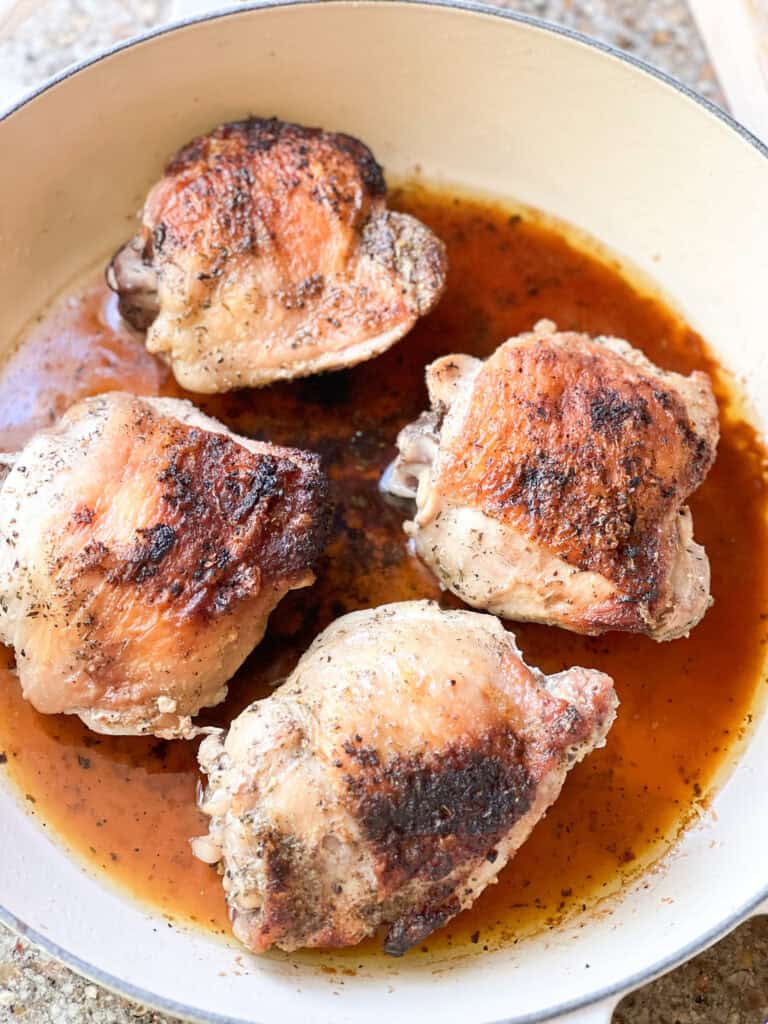 Portrait photo of 4 bone-in chicken thighs with skin on that have been roasted until crisp and golden brown for this French Roast Chicken Recipe.