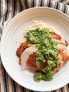 Flatlay photo of overhead shot of a plate of Dry Brine Garlic Herbed Roast Turkey Breast served atop a bed of cauliflower puree and a seasonal green pesto.