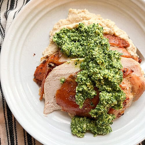 Flatlay photo of overhead shot of a plate of Dry Brine Garlic Herbed Roast Turkey Breast served atop a bed of cauliflower puree and a seasonal green pesto.