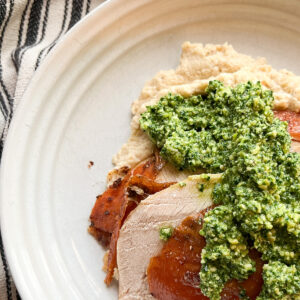 Flatlay photo of overhead shot of a plate of Dry Brine Garlic Herbed Roast Turkey Breast served atop a bed of cauliflower puree and a seasonal green pesto.