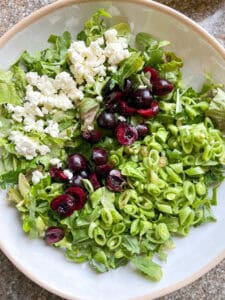 Flatlay photo of finished Cherry Arugula Salad with Honey Lemon Dressing Recipe. The salad is arranged with rows of feta, cherries, and slice snap peas before tossing with the dressing.