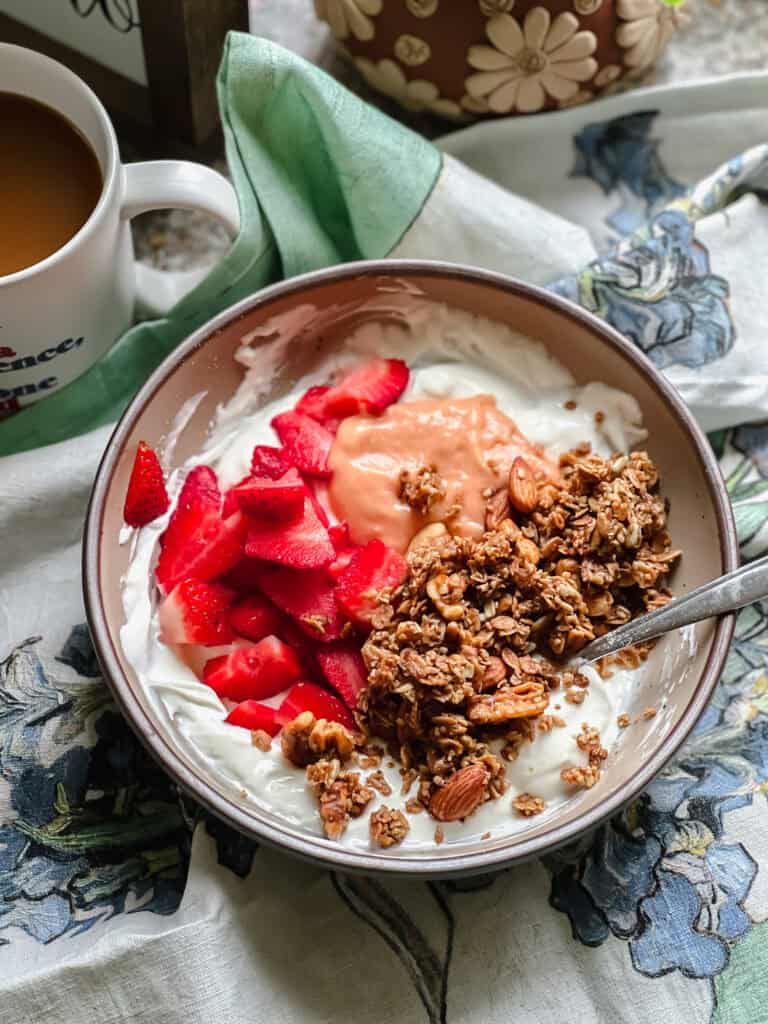 Portrait photo of a bowl of yogurt topped with Rhubarb Curd, fresh strawberries, and homemade granola.