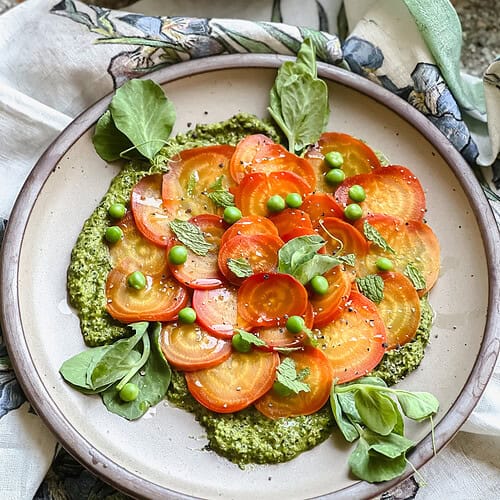 Flatlay photo showing the finished Vegan Roasted Badger Flame Shaved Beet Salad Recipe. Pops of green beet greens pesto and English peas accent the bright orange and yellow swirls of color found on this golden beet variety.