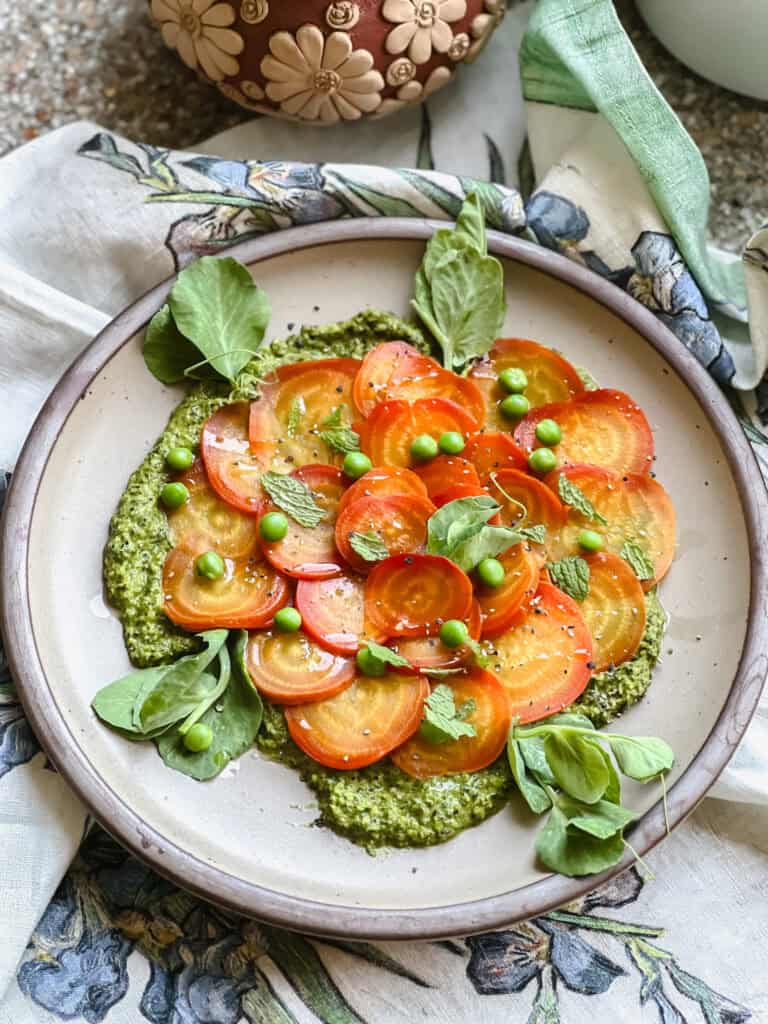 Flatlay photo showing the finished Vegan Roasted Badger Flame Shaved Beet Salad Recipe. Pops of green beet greens pesto and English peas accent the bright orange and yellow swirls of color found on this golden beet variety.