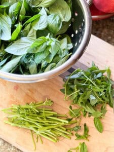 Flatlay photo of the various parts of the basil bunch: stems, leaves, and smaller leaves. The plant has been picked apart for multiple recipes to prep.