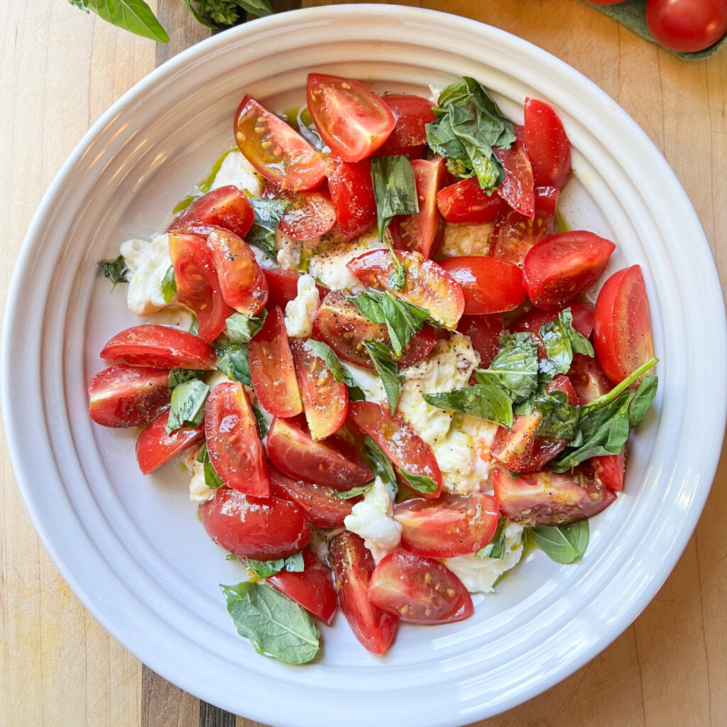 Finished photo of a shallow bowl holding a family size serving of Caprese Salad with Cherry Tomatoes and Basil Oil.