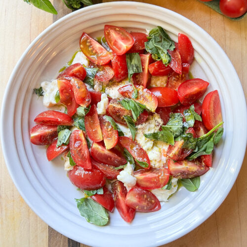 Finished photo of a shallow bowl holding a family size serving of Caprese Salad with Cherry Tomatoes and Basil Oil.