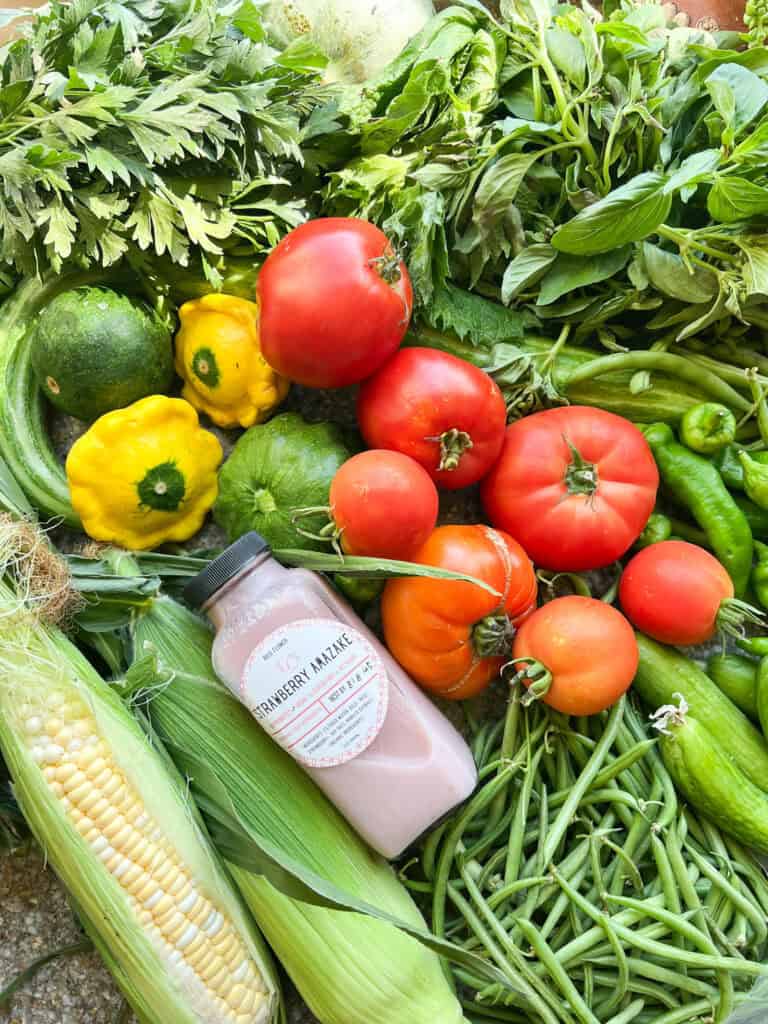 Flatlay photo of summertime produce for Dinner Plans Week 32 featuring tomatoes, summer squash, corn, green beans, shiso, basil, cucumbers. 