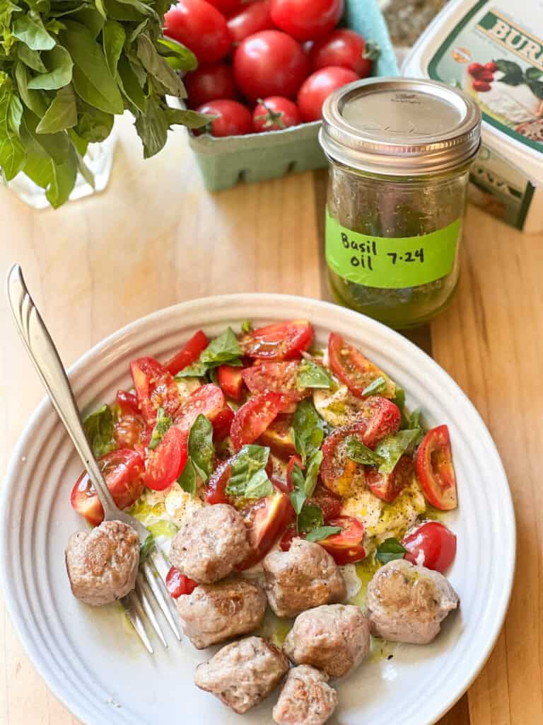Photo of Caprese Salad with Cherry Tomatoes and Basil Oil served alongside turkey meatballs. A small jar of basil oil is off set in the upper right corner of the photo. 
