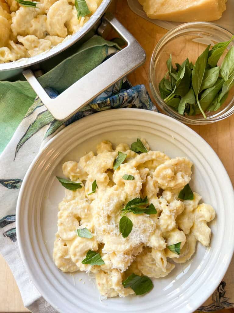 Portrait photo of finished Creamy Corn pasta dish garnish with fresh basil leaves. A generous portion is served in a shallow pasta bowl. 