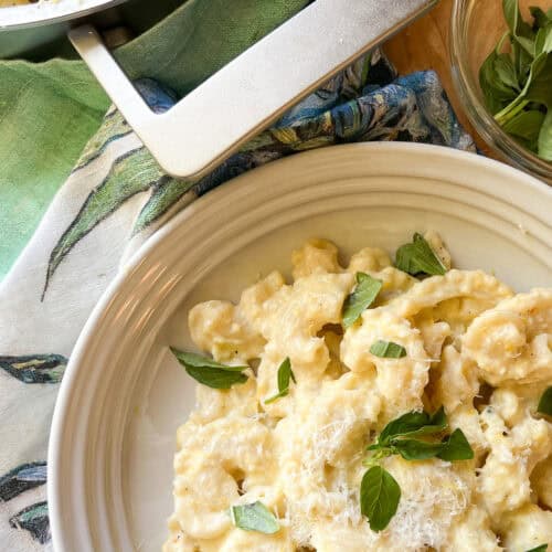 Portrait photo of finished Creamy Corn pasta dish garnish with fresh basil leaves. A generous portion is served in a shallow pasta bowl.