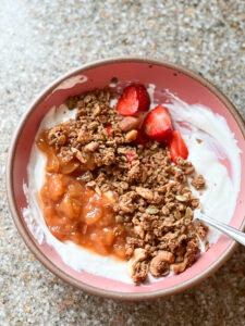 A bowl of yogurt with swirls of peach compote with granola and fresh fruit.