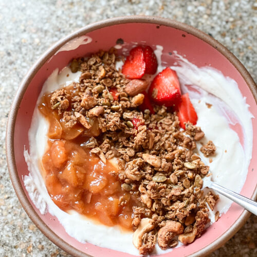 A bowl of yogurt with swirls of peach compote with granola and fresh fruit.