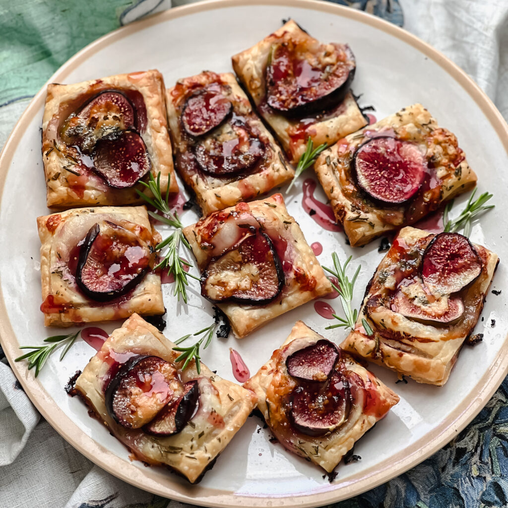Flatlay photo of the finished Fig and Blue Cheese Appetizers on a white plate set over a floral patterned napkin. 