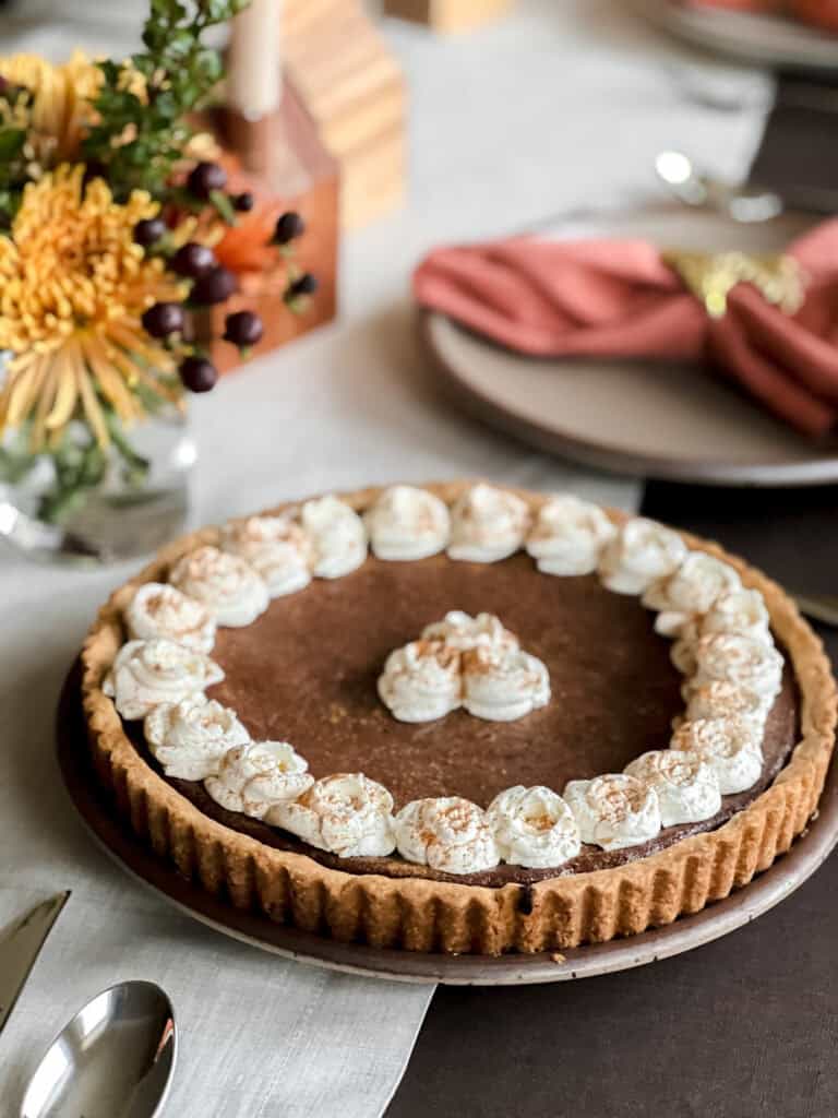Portrait photo of Persimmon Butter Tart Recipe sitting atop a table decorated for the Thanksgiving season. 