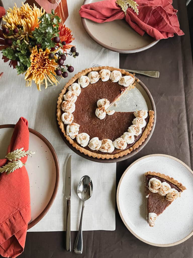 Flatlay photo of a single slice of the Persimmon Butter Tart atop a dessert plate adjacent to the full tart. 