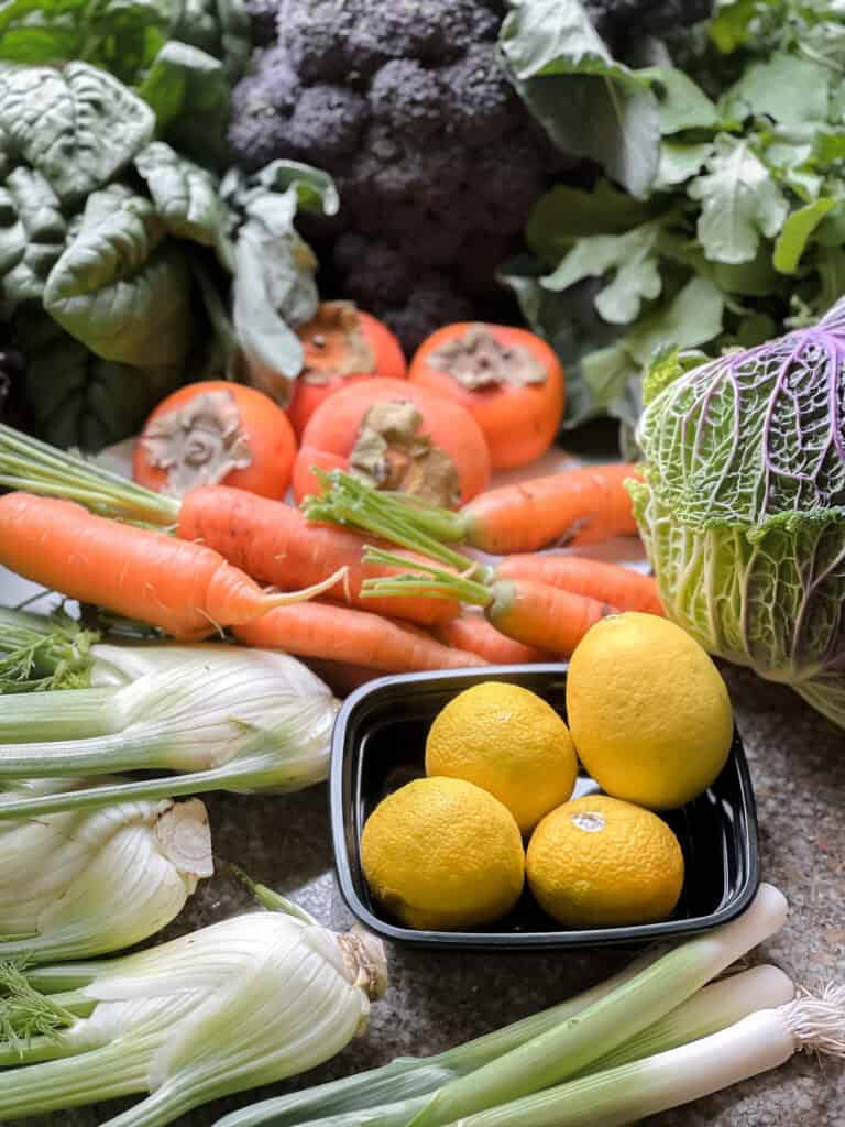 Portrait photo of late autumn produce for Dinner Plans Week 50 featuring fennel, yuzu, carrols,  persimmons, savoy cabbage, sprouting broccoli, and spinach. 