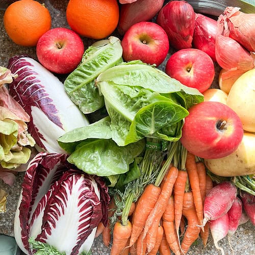 Flatlay photo of seasonal produce for Dinner Plans Week 5 featuring radicchio, carrots, apples, mandarins, leeks, and potatoes.
