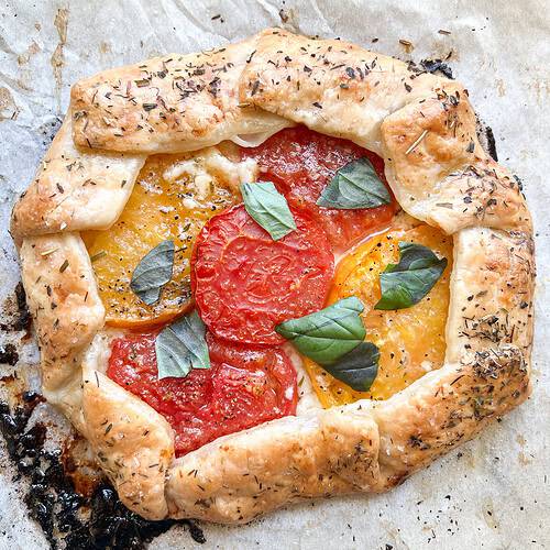 Flatlay photo of the finished Heirloom Tomato Galette garnished with fresh torn basil leaves.