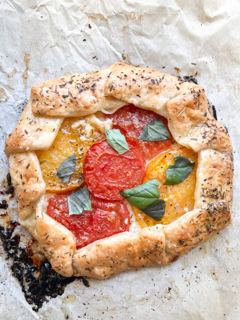 Flatlay photo of the finished Heirloom Tomato Galette garnished with fresh torn basil leaves. 