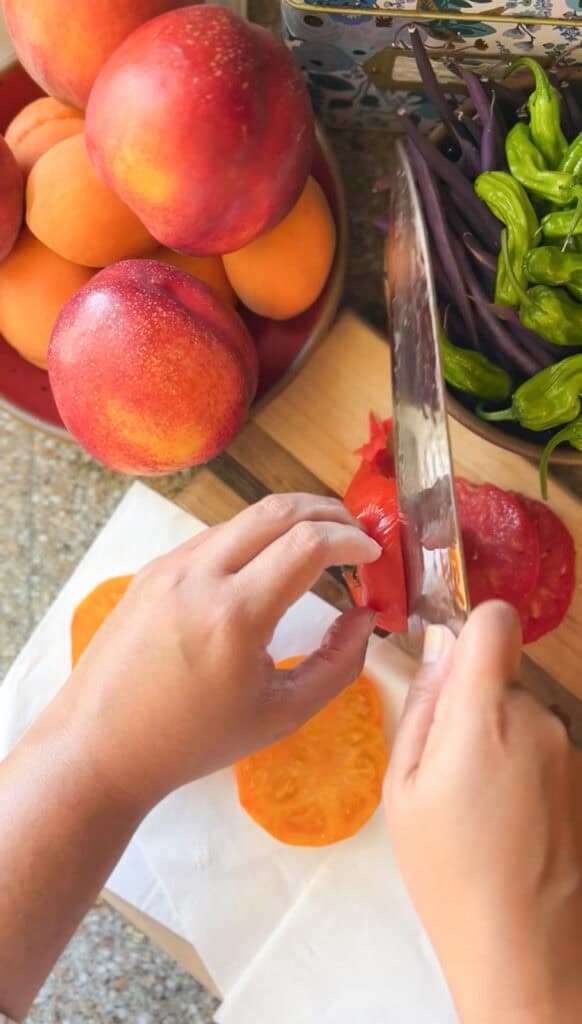 two hands are seen slicing heirloom tomatoes into ½ inch slices. 