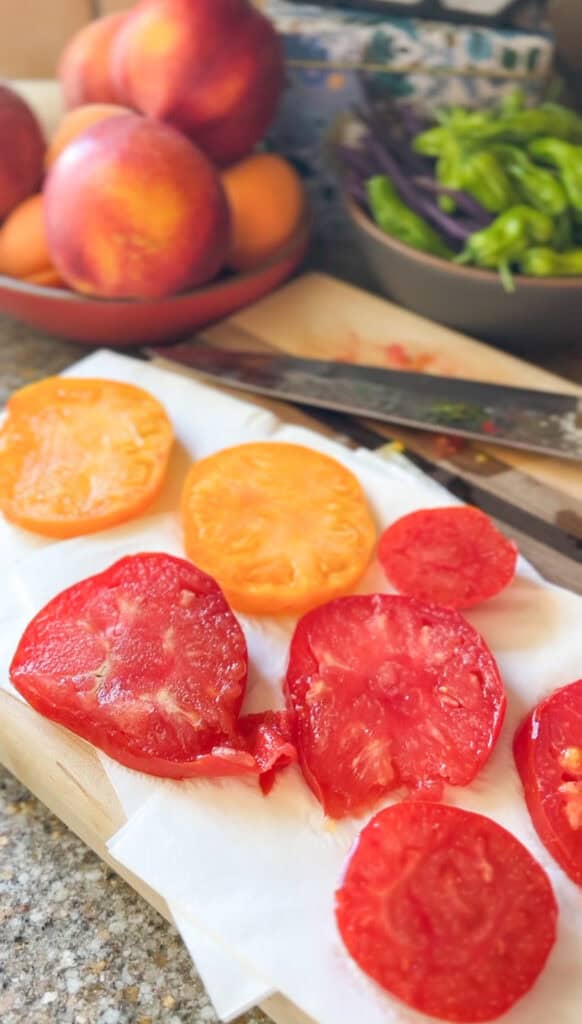 Layers of heirloom tomato slices are seasoned with kosher salt and ground black pepper and drain excess moisture on a paper towel lined plate. 