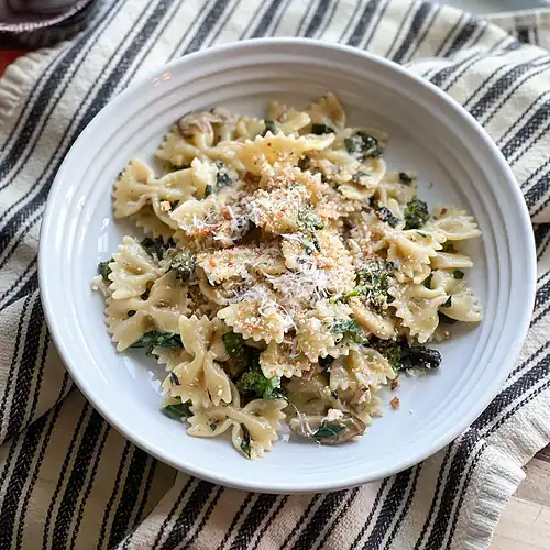 Flatlay portrait of the Late Winter Pasta with Mushrooms, Kale and Sprouting Broccoli garnished with a generous grate of parmesan cheese.