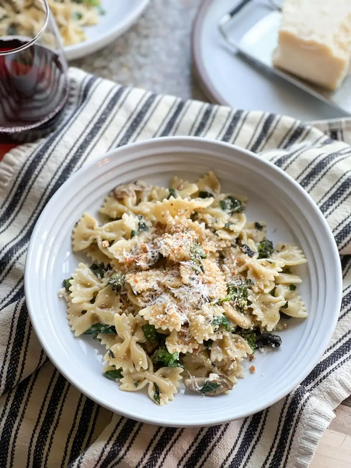 Flatlay portrait of the Late Winter Pasta with Mushrooms, Kale and Sprouting Broccoli garnished with a generous grate of parmesan cheese.