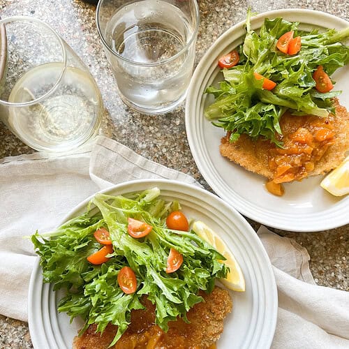 Photo of finished dish of Thin Pork Cutlets recipe with seasonal summer salad with frisee and tomatoes.