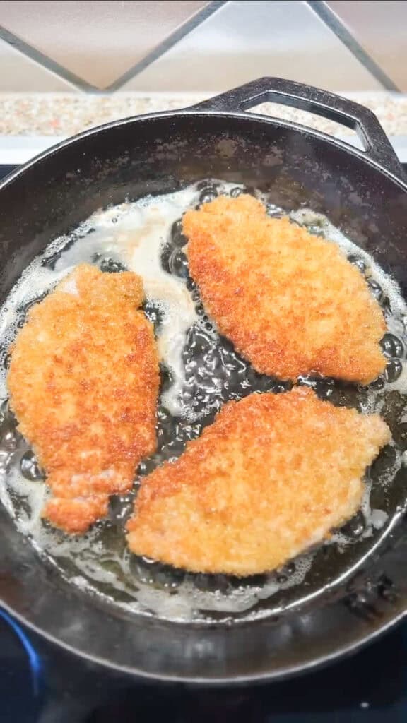Overhead photo of thin pork cutlets being shallow fried in a cast iron skillet.