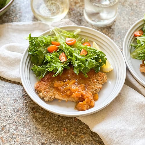 Photo of finished dish of Thin Pork Cutlets recipe with seasonal summer salad with frisee and tomatoes.