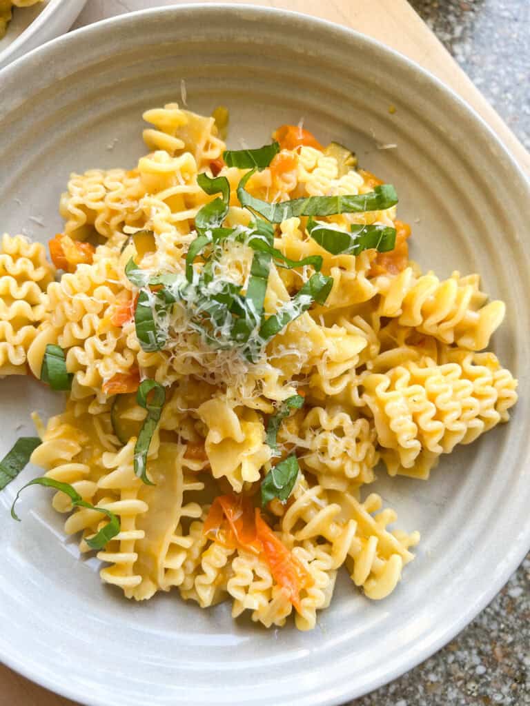 Close up of Sun Gold Tomato Pasta with fresh basil leaves on a white ceramic shallow bowl.