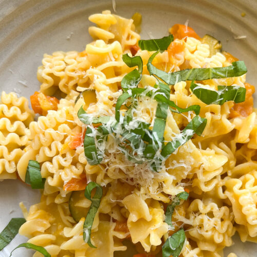 Close up of Sun Gold Tomato Pasta with fresh basil leaves on a white ceramic shallow bowl.