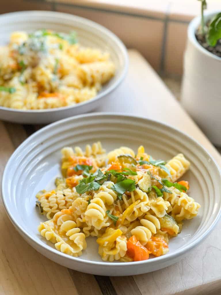 Sun Gold Tomato Pasta with fresh basil leaves on a white ceramic shallow bowl.