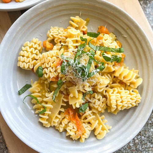 Sun Gold Tomato Pasta with fresh basil leaves on a white ceramic shallow bowl.