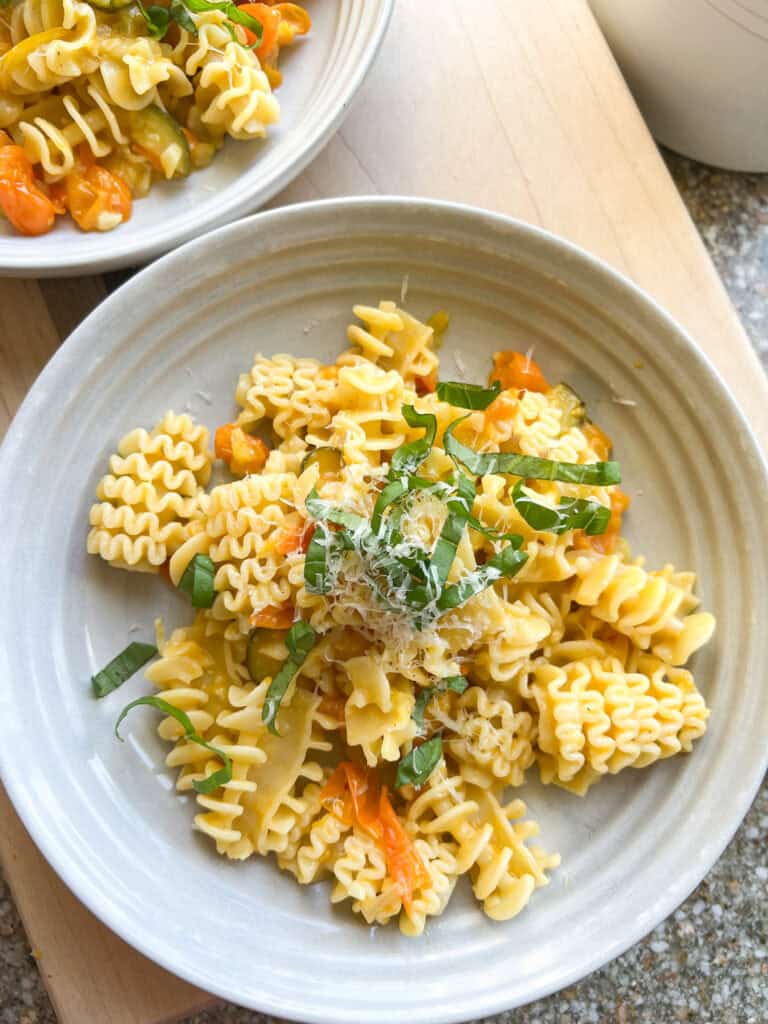 Sun Gold Tomato Pasta with fresh basil leaves on a white ceramic shallow bowl. 