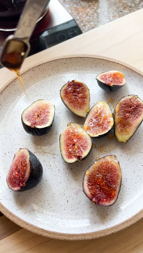Plate of halved figs drizzled with honey prior to cooking.