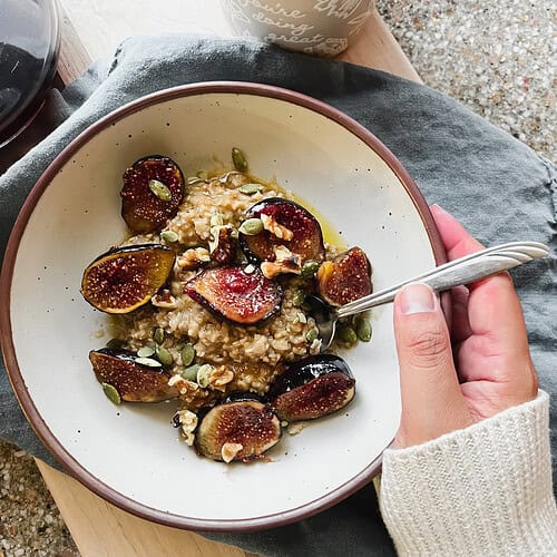 overhead photo of a woman's hand holding a bowl of oats topped with caramelized figs.